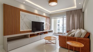 A modern living room with a large TV, wooden panel wall, a sofa, and a coffee table. - Sofisticação e Conforto Città Life (Florianópolis)