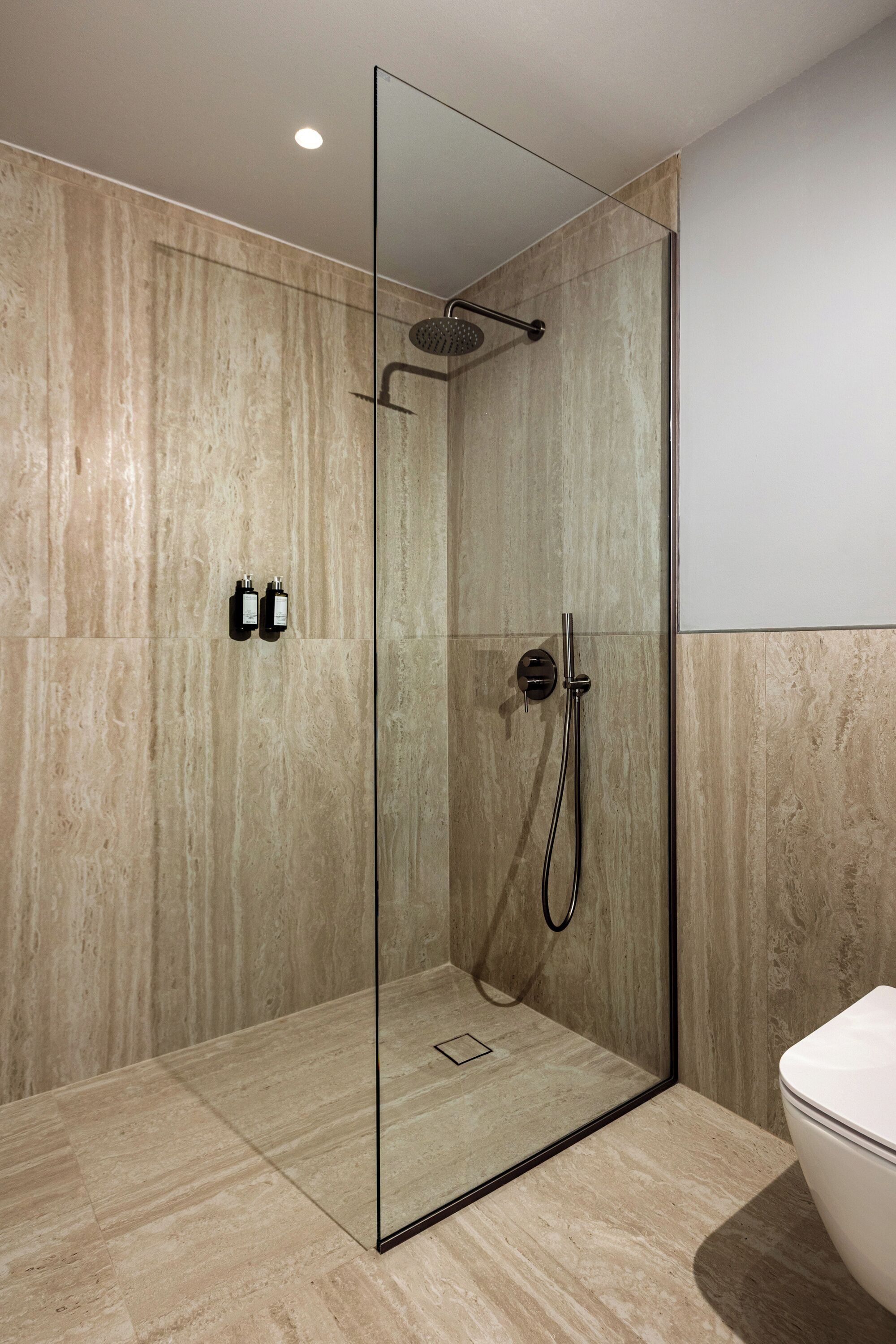 A modern bathroom with a glass-enclosed shower, a white toilet, and marble walls.