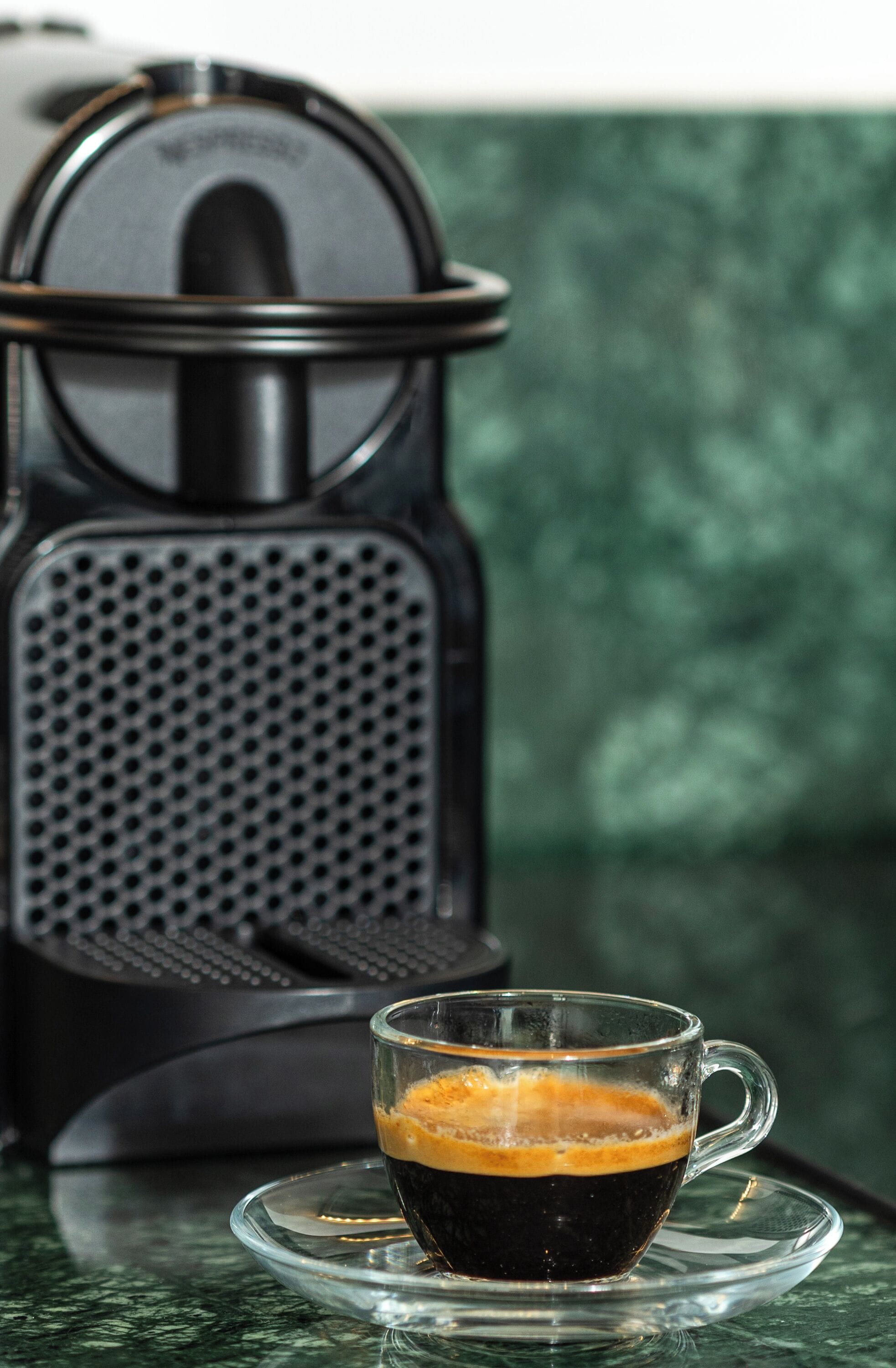 En kaffemaskine og en kop kaffe på et glastilbords.