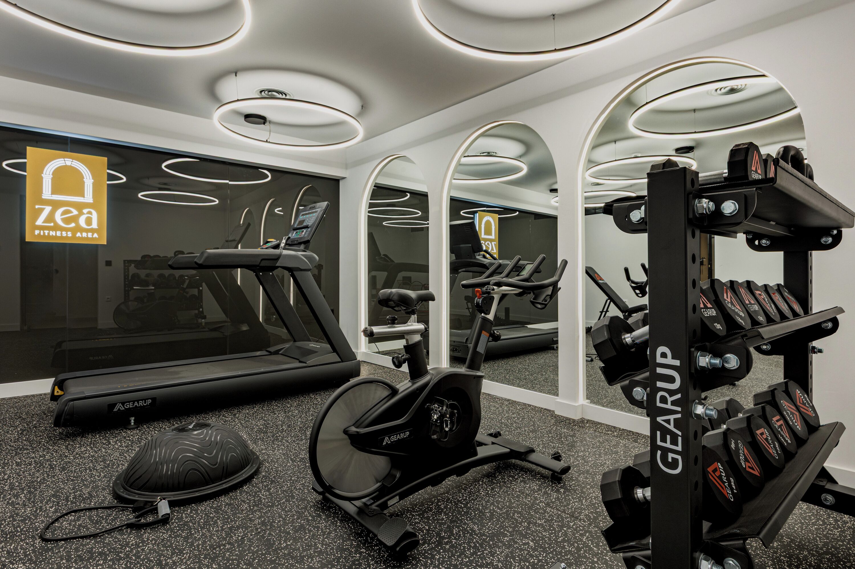 A modern fitness area with a treadmill, stationary bike, and weightlifting equipment.