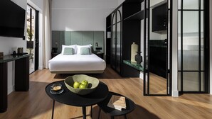 A modern hotel room with a large bed, a dining area with a table and chairs, a kitchen area, and a large window. - Zea Urban Living (Piraeus)