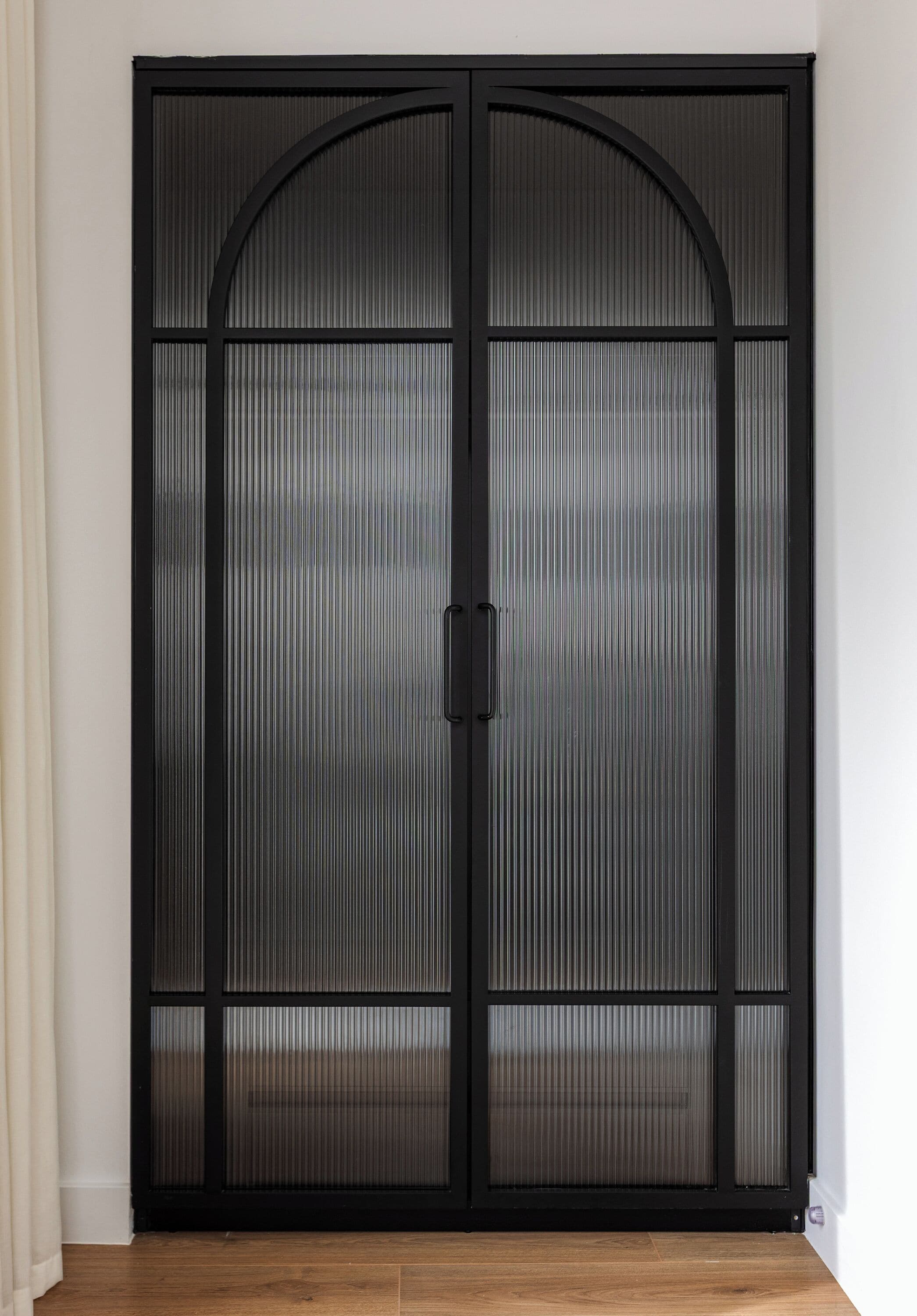 A black sliding door with a handle, a wooden floor, and a white wall.