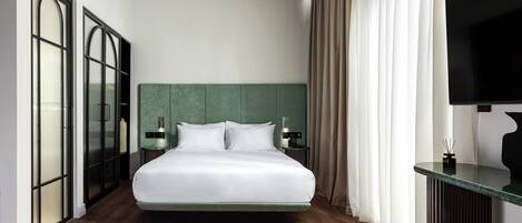 A modern hotel room with a large bed, a flat-screen TV, a green headboard, and a wooden floor.