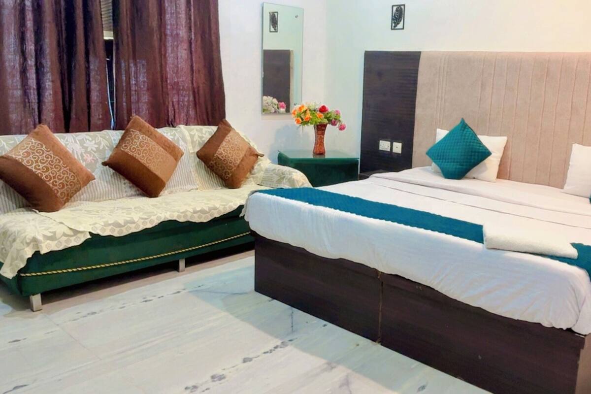 A bedroom with a green sofa set, a large bed with a blue accent, and a small table with a vase of flowers.