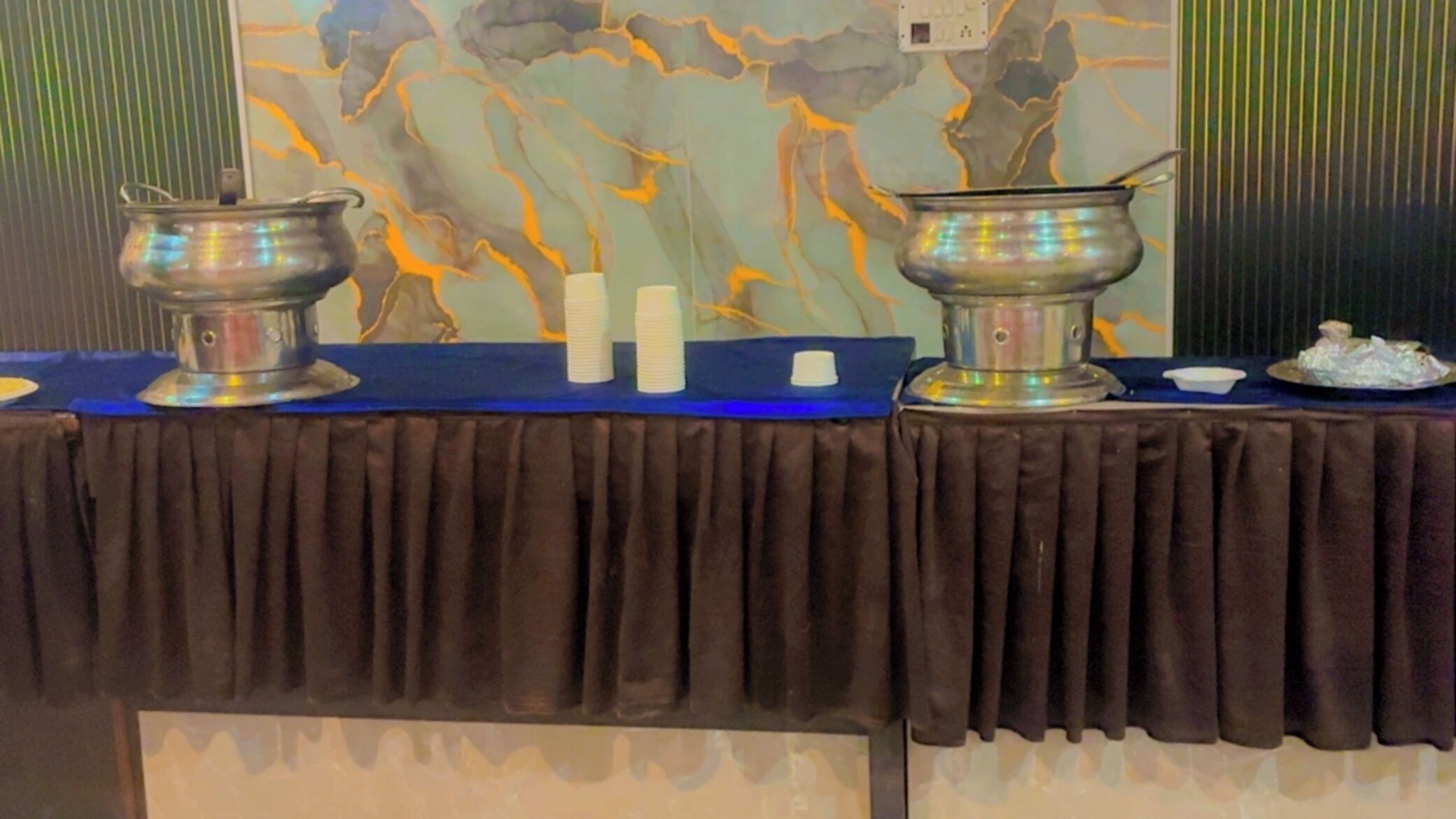 Ein Tisch mit zwei Metallbehältern, einer blauen Tischdecke und einer dekorativen Wand im Hintergrund.