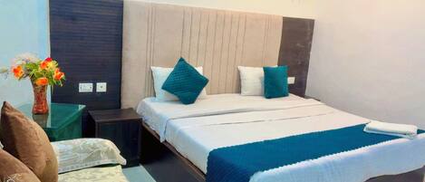 A hotel room with a bed, bedside tables, a nightstand, a vase with flowers, and a chair.