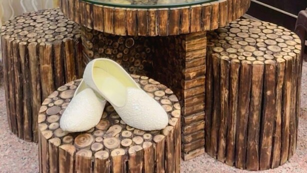 A room with a round glass table surrounded by wooden stools, a decorative figure on the table, and a pair of slippers on one stool. - Hotel Taj Signature (Agra)