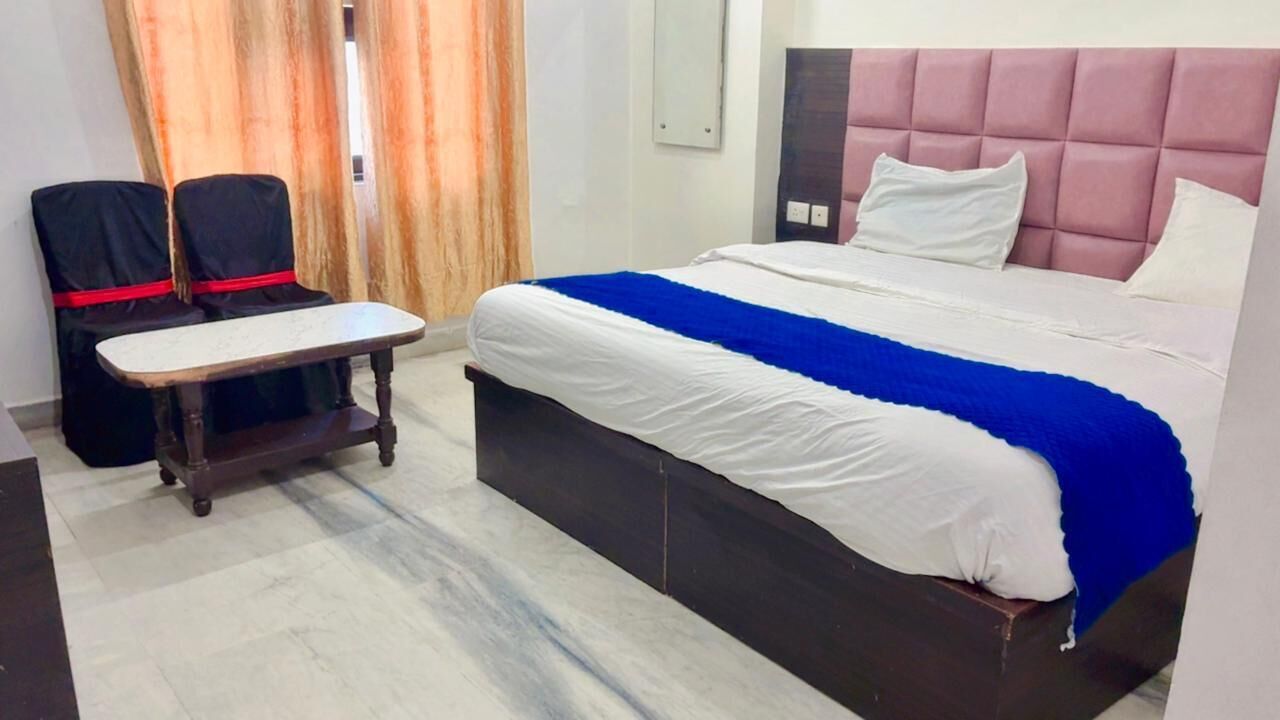 A hotel room with a bed, a small table, two chairs, and a window with curtains.