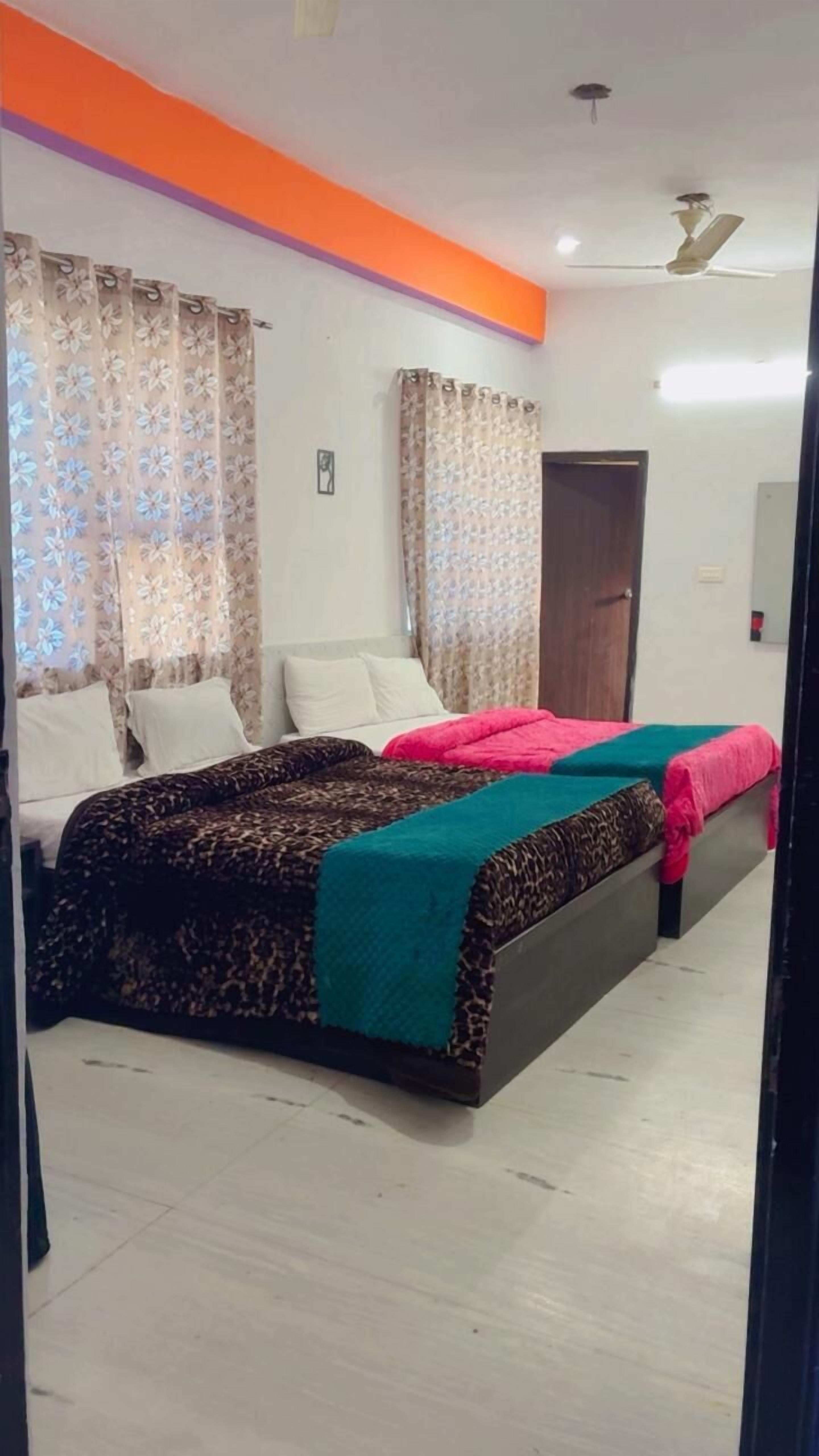 A bedroom with two beds, floral curtains, a ceiling fan, and a door.