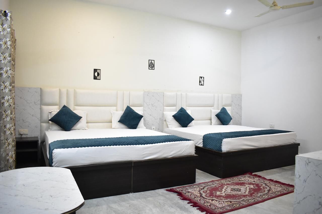 A hotel room with two beds, a marble-topped table, a red and beige patterned rug, and a ceiling fan.