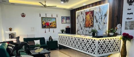 Zona de recepción con una lámpara moderna, mostrador de recepción, asientos verdes y una pared decorativa con cuadros enmarcados.