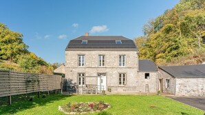 A stone building with a sloped roof, a small garden, and a wooden fence. - A Fleur de l'Eau Blanche: character gîte (Chimay)