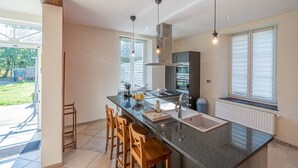 A modern kitchen with a central island, bar stools, pendant lighting, and a view of the backyard. - A Fleur de l'Eau Blanche: character gîte (Chimay)