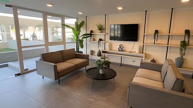 Una sala de estar moderna con un sofá, sillones, una mesa de centro y un televisor. Hay plantas y estantes con objetos decorativos.