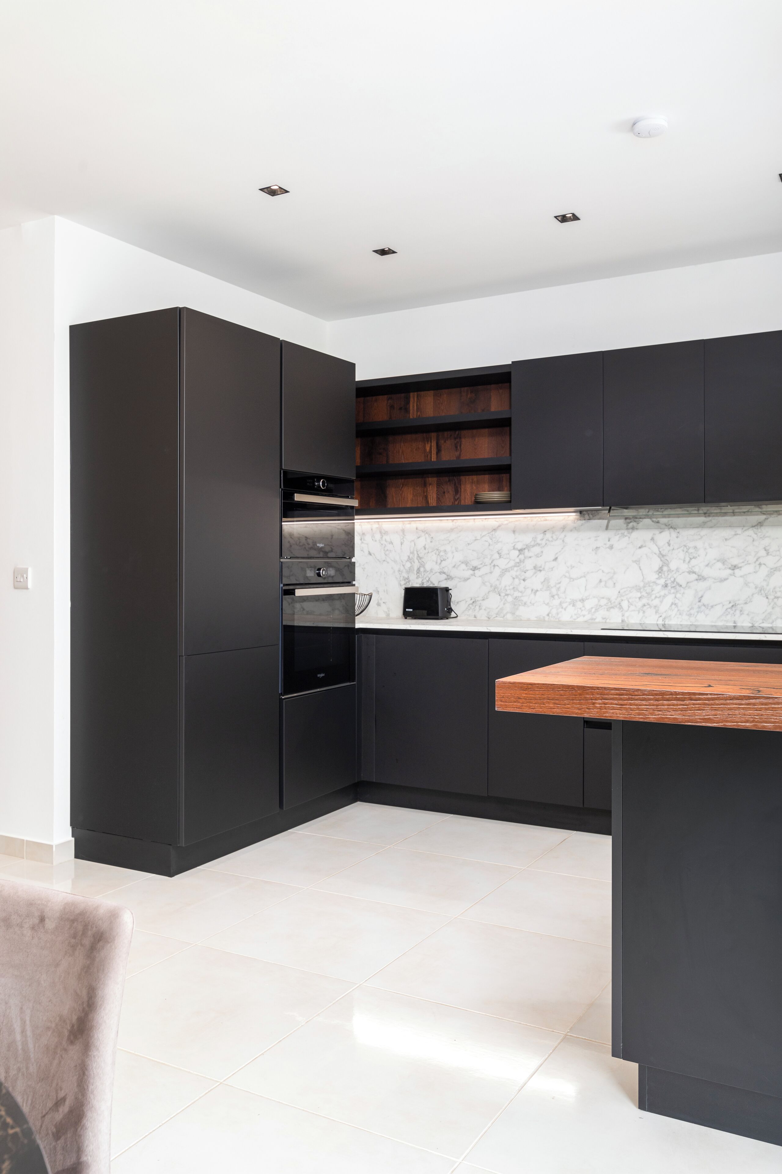 A modern kitchen with dark cabinetry, a marble countertop, and a wooden island.