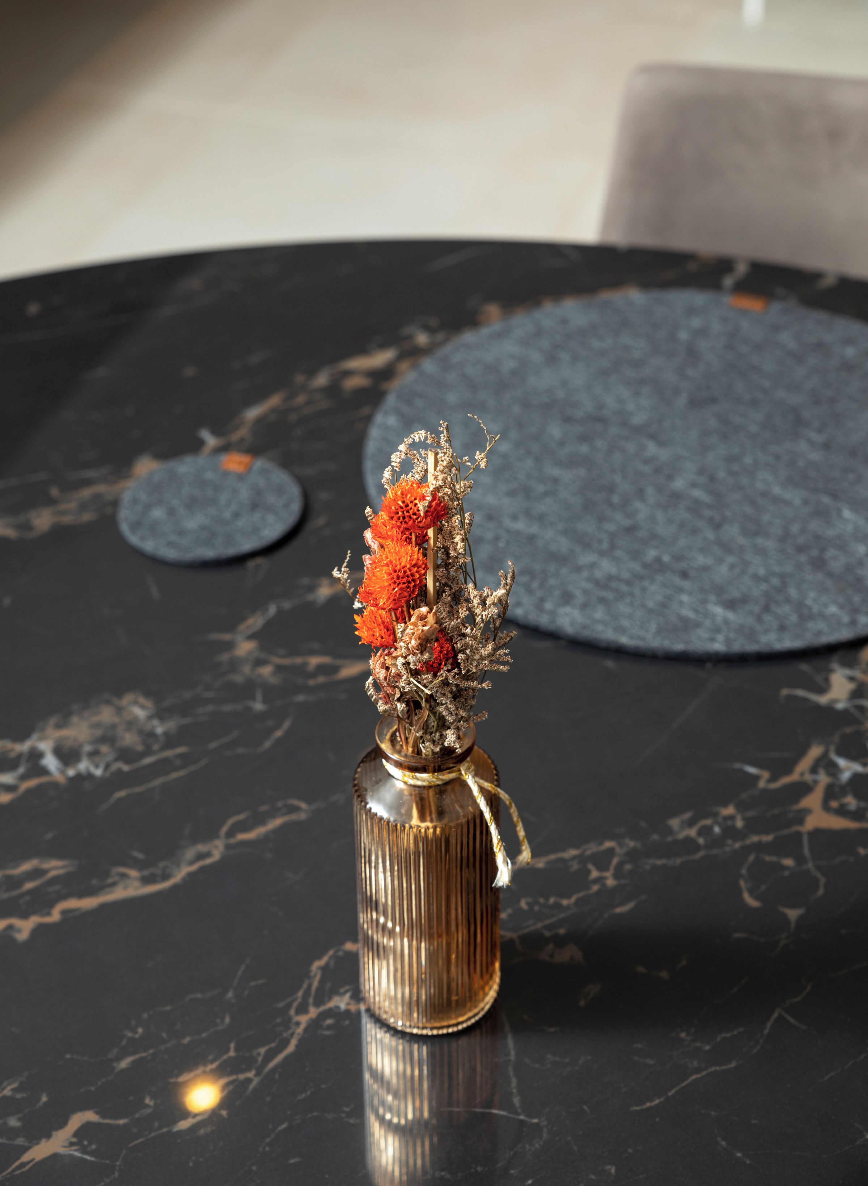 A marble table with a vase of dried flowers and a round placemat.