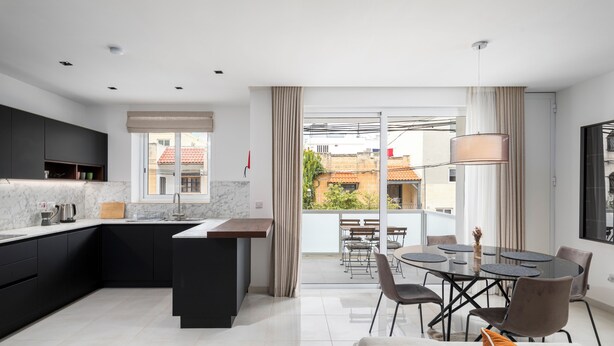 A modern kitchen with a central island, a dining area with a round table, and a balcony with a view of buildings. - Modern Stylish 3 BR APT with Balcony (Swieqi)