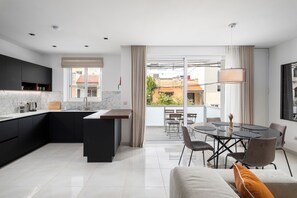 Een moderne keuken met een centraal eiland, een eetgedeelte met een ronde tafel, en een balkon met uitzicht op gebouwen.