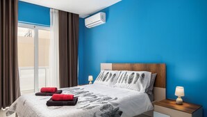 A hotel room with a bed, a nightstand, a lamp, and an air conditioning unit. - Modern Stylish 3 BR APT with Balcony (Swieqi)