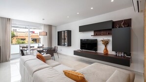 A modern living room with a sofa, TV, and a dining area with a table and chairs. - Modern Stylish 3 BR APT with Balcony (Swieqi)