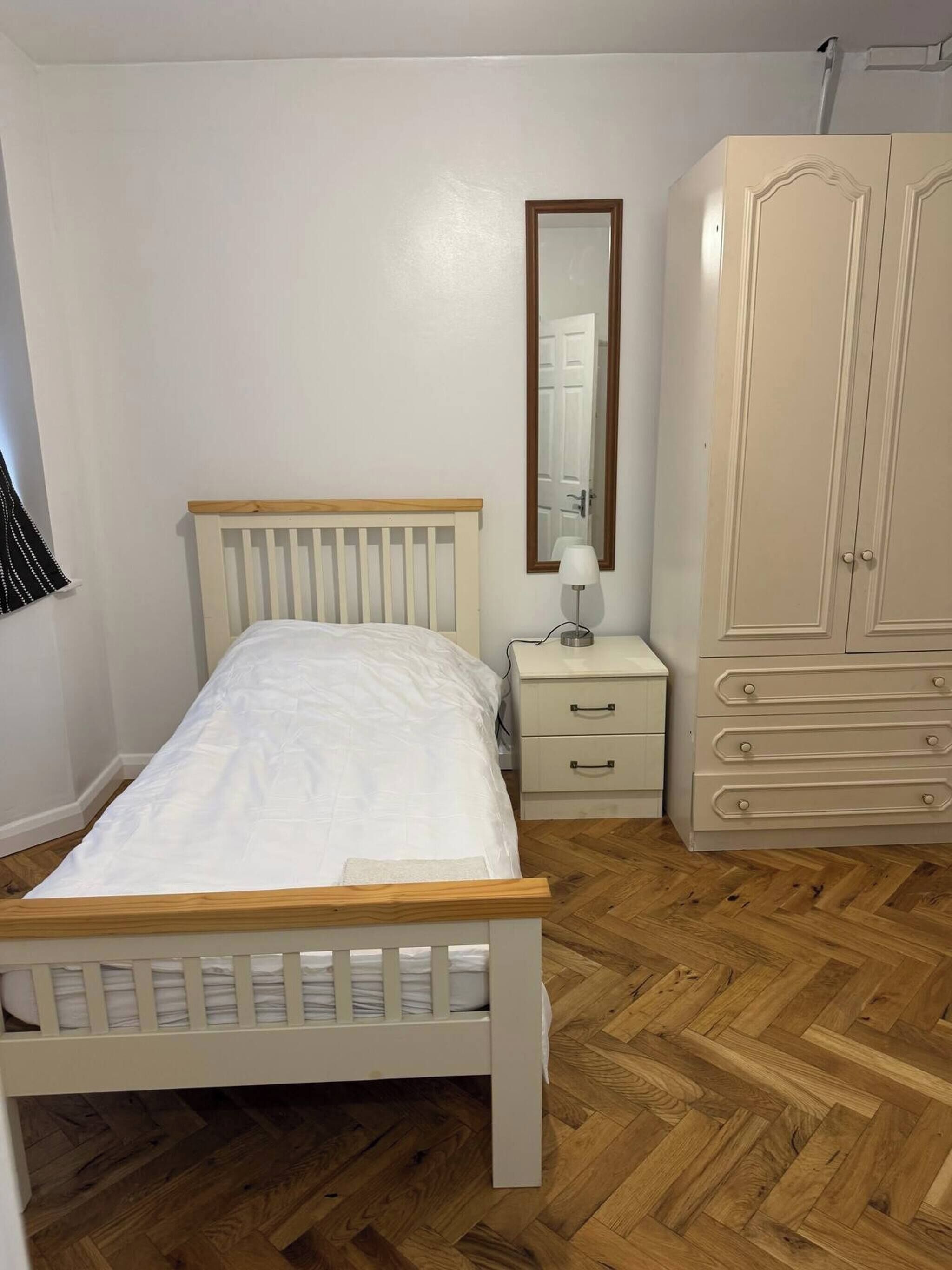 A bedroom with a wooden bed, a nightstand, a dresser, and a mirror.