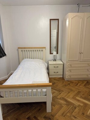 A bedroom with a wooden bed, a nightstand, a dresser, and a mirror. - Spacious 4-bedroom Home in Ashford, Kent - Perfect for Families and Groups (Ashford)