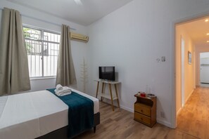 Un dormitorio con cama, televisor, una mesita y suelo de madera.