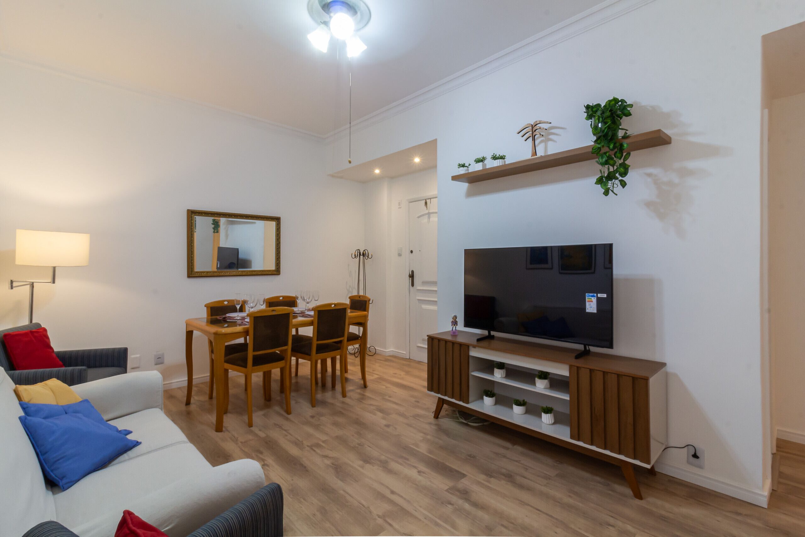 Sala de estar con sofá, mueble para televisión, mesa de comedor, sillas y una planta.