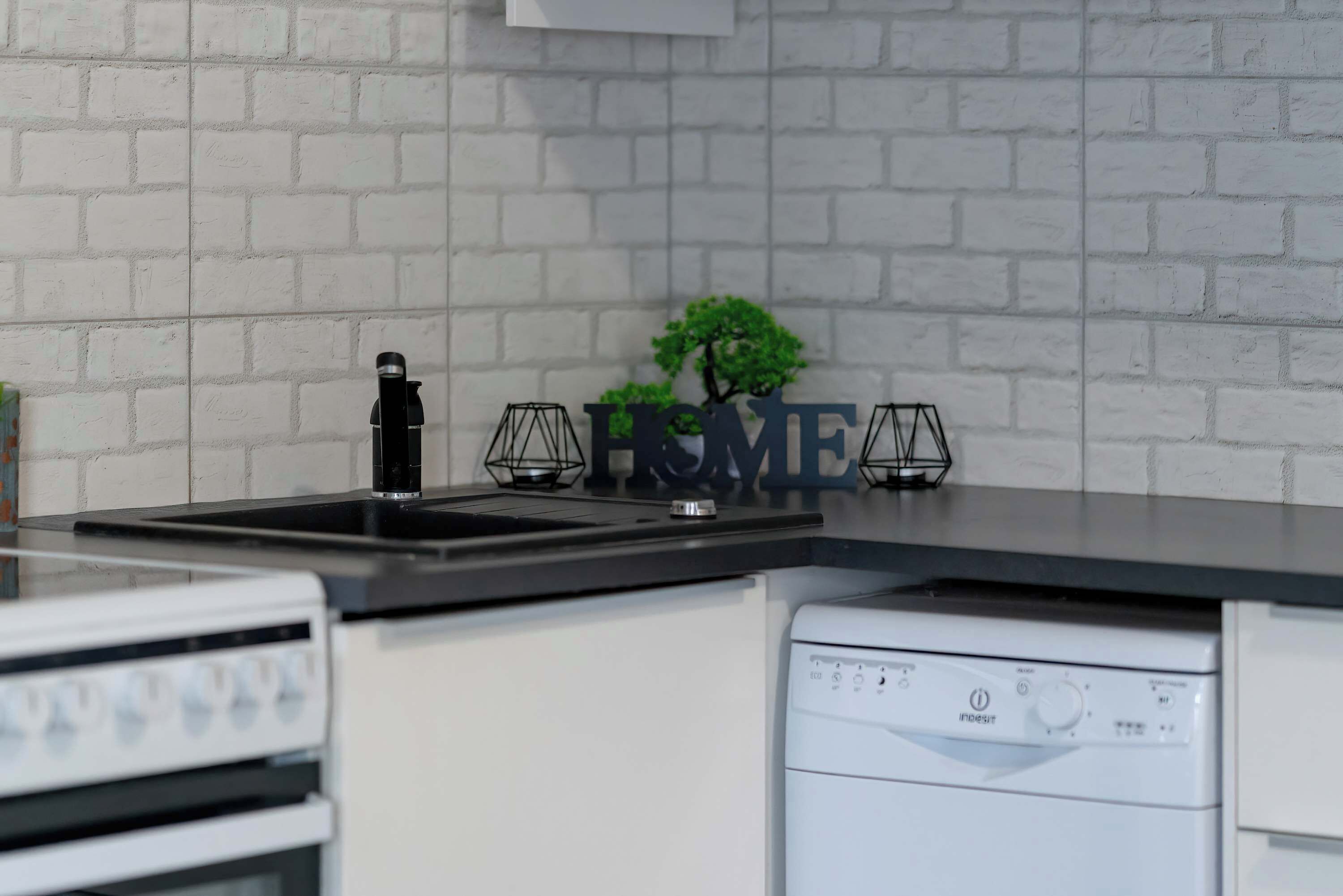 Una cocina con protector mural de ladrillo blanco, encimera negra, un lavabo, una estufa y un lavavajillas.