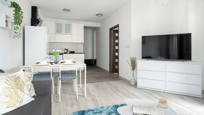 Un soggiorno moderno con un divano, un tavolino e una TV. È presente anche un angolo cottura con un tavolo da pranzo e sedie.