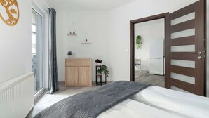 Una camera da letto moderna con un letto, un armadietto in legno, una piccola pianta e una porta che dà su un'altra stanza.