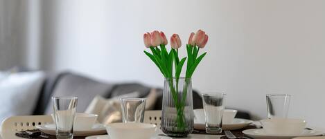 Una mesa de comedor puesta con platos, tazones, vasos y un florero con flores.
