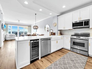 A modern kitchen with white cabinetry, stainless steel appliances, and a large island. - Adagio E-303 - NEW to program for 2026! (Santa Rosa Beach)