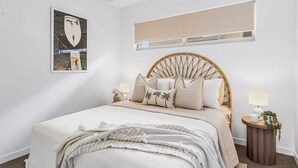 Ein Schlafzimmer mit einem Bett, Kissen, einem Nachttisch mit Lampe, einer Wand-Klimaanlage und einem gerahmten Bild an der Wand.