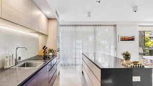 Eine moderne Küche mit einer eleganten Kochinsel, Edelstahlgeräten und einem großen Fenster mit durchscheinenden Vorhängen.