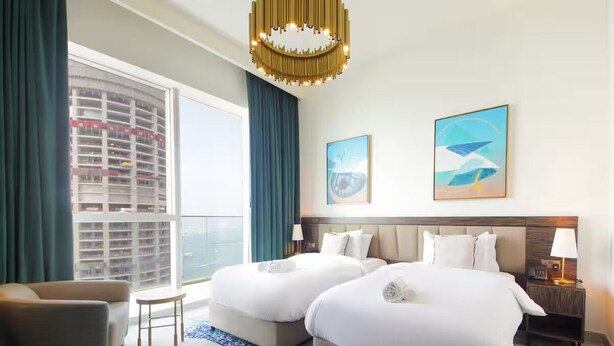 Une chambre d’hôtel avec deux lits, un canapé, une petite table et une vue sur un immeuble de grande hauteur.