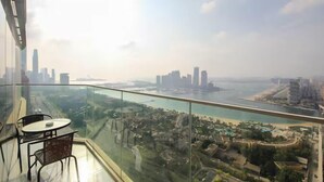 Un immeuble de grande hauteur doté d’un balcon en verre offrant une vue panoramique sur le paysage urbain côtier, notamment sur un port de plaisance et des bâtiments de la ville.