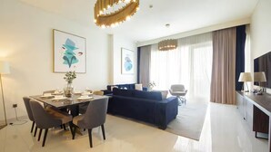 Une chambre d’hôtel moderne dotée d’un coin repas, d’un canapé, d’une télévision et d’une grande fenêtre avec des rideaux.