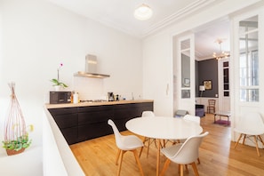 A modern kitchen with white cabinetry, a central island, and a dining area with white chairs. - Comfortable Central And Quiet (Brussels)