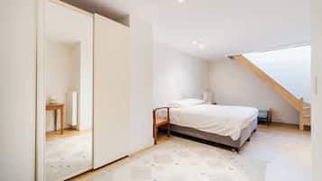 Une chambre à coucher avec un lit, un miroir, une chaise en bois, une petite table et un escalier.