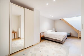 Un dormitorio con cama, espejo, silla de madera, mesita y una escalera.