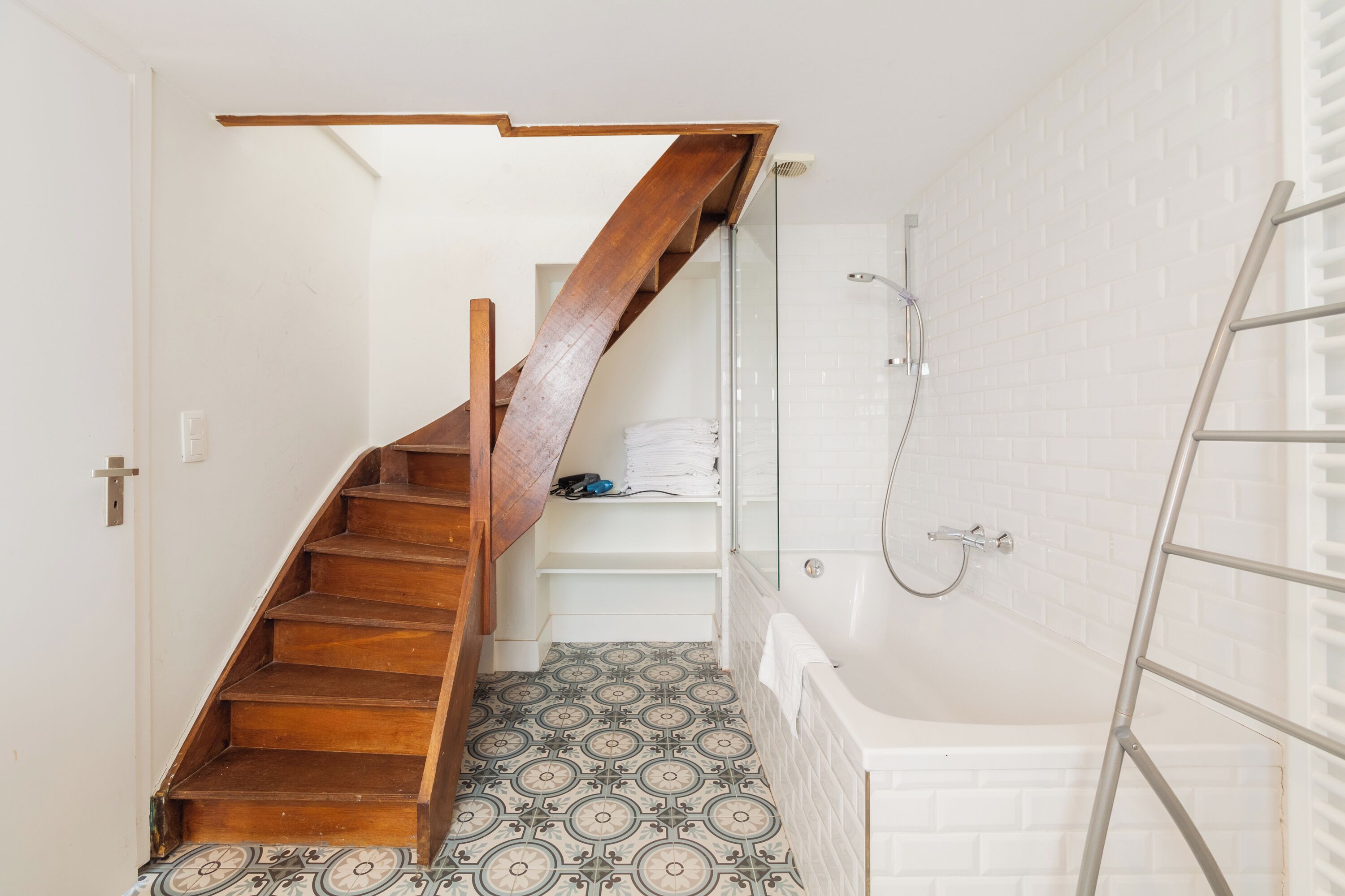 Une salle de bain avec un escalier en bois, une douche et des carreaux de sol à motifs.