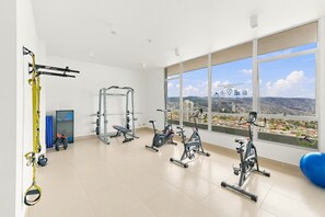 A gym with various exercise equipment, a yoga ball, and a view of a cityscape through large windows. - Oceana Suites Cerro Placeres (Valparaiso)