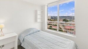 A bedroom with a bed, a desk, a lamp, and a window with a city view. - Oceana Suites Cerro Placeres (Valparaiso)