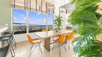 Un comedor moderno con una mesa grande y sillas, ventanas amplias con vista a la ciudad y una planta en maceta.