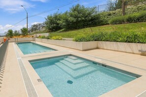 Two rectangular swimming pools with clear blue water, surrounded by a low wall and a grassy area with trees. - Oceana Suites Cerro Placeres (Valparaiso)