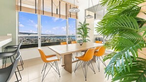 A modern dining area with a large table and chairs, large windows with a city view, and a potted plant. - Oceana Suites Cerro Placeres (Valparaiso)