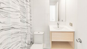 A bathroom with a marble-patterned shower curtain, a white toilet, a sink with a mirror above it, and a wooden cabinet below. - Oceana Suites Cerro Placeres (Valparaiso)