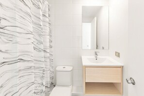 A bathroom with a marble-patterned shower curtain, a white toilet, a sink with a mirror above it, and a wooden cabinet below. - Oceana Suites Cerro Placeres (Valparaiso)