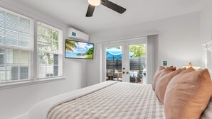 Ein Schlafzimmer mit einem Bett, einem Deckenventilator, einem Fernseher und Blick ins Freie.